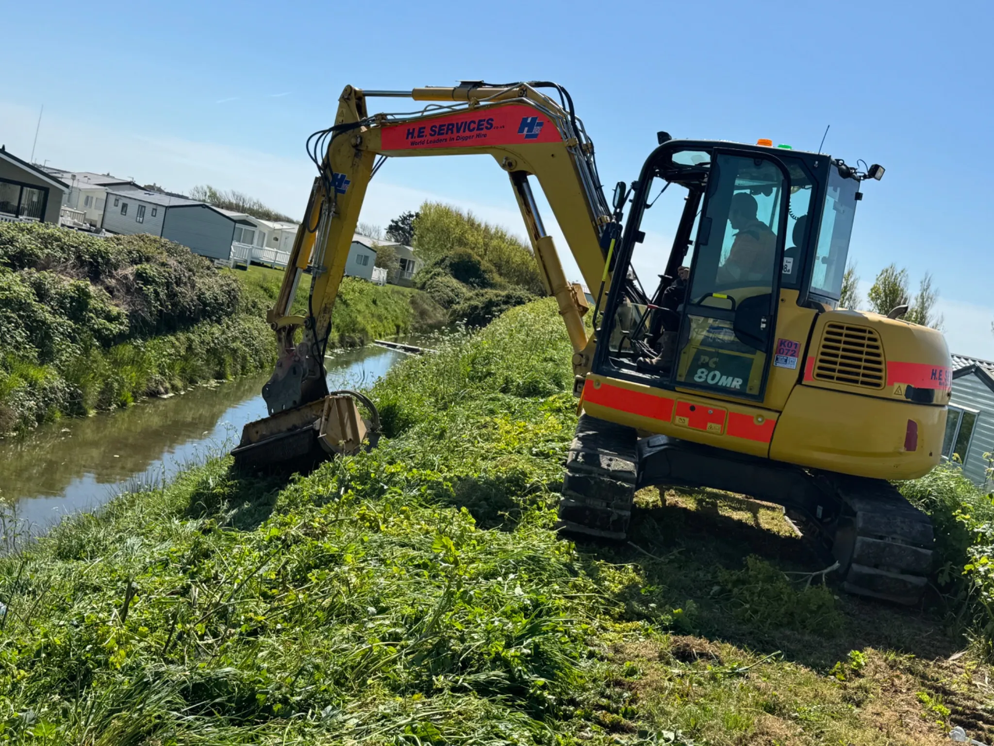 Tracked excavator carrying out vegetation clearance beside a waterway